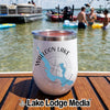A white insulated wine tumbler featuring a Walloon Lake, Michigan map graphic rests on a wooden boat deck with people swimming in the background.