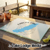 A glass cutting board with a blue map of Carlyle Lake and compass graphic rests on a wooden dock with copper mugs and lime slices.