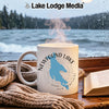 White mug with Newfound Lake map and compass on table with book and scarf.