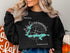 Black sweatshirt with "Lake Ossawinamakee Minnesota" text and compass graphic.