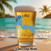 Beer glass with "Forest Lake" text and compass on a beach at sunset.