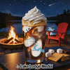 Glass of layered drink with ice cream, near campfire and s'mores ingredients.