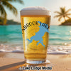 Glass of beer with "LINBROOK LAKE" map design on a beach at sunset.