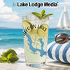 Tall glass of lemonade with lime slices and mint on a beach with a sailboat.