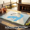 A glass cutting board featuring a blue map of Augur Lake and compass design on a wooden table.