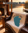 Woven blanket with Hauser Lake, Idaho design draped over a leather couch by a fireplace.