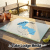 A rectangular glass cutting board with a blue Forest Lake, Minnesota map design sits on a wooden outdoor bar.