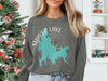 A person wears a gray sweatshirt featuring a turquoise map and compass with "Shaver Lake California" printed on it.