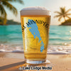 Beer glass with Lake Winnipeg map and compass on a beach with palm trees.