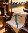 Woven blanket with Otisco Lake map and compass, draped on a leather armchair.