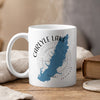 White mug with blue Carlyle Lake map and compass graphic, steaming.