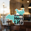 Aqua map outlines with black text "Brooks Hess Life" on glass.