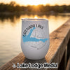 A white insulated wine tumbler featuring a blue map of Grenada Lake, Mississippi, sits on a wooden dock overlooking a lake at sunset.