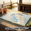 A glass cutting board rests on a wooden table with a map of Lake Wateree, South Carolina, a compass rose, and two copper mugs in the background.