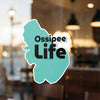 Teal sticker with text "Ossipee Life" overlaid on a window.