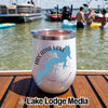 A white insulated tumbler featuring an Arcadia Lake map design, sitting on a wooden boat deck with people swimming in the lake background.