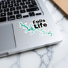 Turquoise lake outline sticker with black text "Falls Life" on laptop keyboard.
