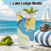 Glass with drink, lime, and mint on a beach with a sailboat.