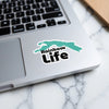 Sticker with "Rainbow Life" text and turquoise abstract shape on a laptop.