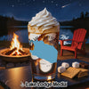 Glass with layered drink and whipped cream next to s'mores ingredients by a campfire.
