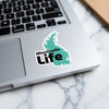 Monticello Life sticker in teal shape of Monticello, placed on a laptop.