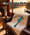 Woven blanket with Barlow Lake and Michigan map design on brown leather couch.