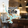 Mitchell Life sticker with lake outline against a blurred background.