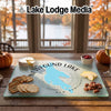 A glass cutting board featuring a map of Newfound Lake, New Hampshire, on a wooden table with snacks.