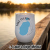 A white insulated wine tumbler featuring a blue map of Lake Pulaski, Minnesota, sits on a wooden dock at sunset.