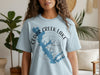 Light blue t-shirt with Cedar Creek Lake outline and compass graphic.