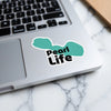 Teal sticker with black text "Pearl Life" on a silver laptop.