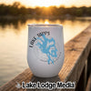 A white insulated wine tumbler featuring a blue lake map and Lake Tapps, Washington text rests on a wooden dock at sunset.