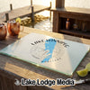 A glass cutting board featuring a blue map of Lake Winnipeg and a compass rose rests on an outdoor wooden table.