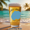 Glass of beer with "Buffalo Lake" and blue shape, beach and ocean background.