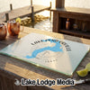 A glass cutting board featuring a blue map of Lake Pend Oreille sits on a wooden dock beside two copper mugs and lime wedges.