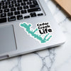 Turquoise sticker of Cedar Creek's outline with "Cedar Creek Life" text on a laptop.
