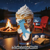Glass with layered drink and whipped cream, surrounded by campfire and s'mores ingredients.
