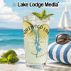 Clear glass with drink, lime, mint, and compass design on beach background.