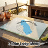 A glass cutting board with an Onondaga Lake design rests on a wooden table outdoors.