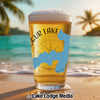 Glass of beer with blue lake shape and compass on beach at sunset