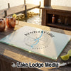A glass cutting board printed with a compass design and Kentucky Lake, resting on an outdoor wooden table.