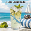 Glass with lake graphic, limes, mint, and ice by the ocean with sailboat.