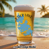 Glass of beer with "Webster Lake Massachusetts" map design on beach background.