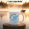 White mug with Squam Lake map and compass on a wooden stump.