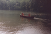 Two people paddling in a canoe on a calm lake with a dense forest shoreline in the background.
