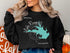 Black sweatshirt with turquoise Lake Rampart map and compass graphic.
