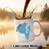White mug with Sebago Lake map, pouring coffee, with a lake and forest background.