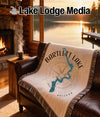 Woven blanket with Bartlett Lake, Arizona map and compass design on a leather sofa.