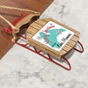 Wooden Christmas ornament on a red sled with "Merry Christmas From Lake Manawa" text.