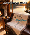 Woven blanket with Hyco Lake and compass design on leather couch.